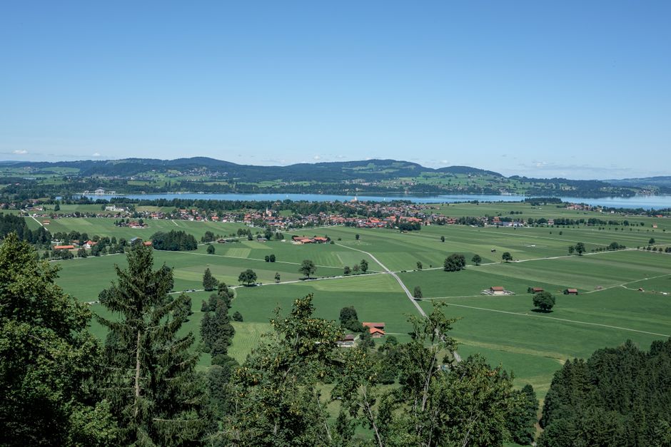 A breathtaking view of the countryside near Füssen, Germany, featuring fields and hills under a clear summer sky.